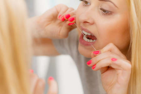 Everyday oral hygiene, dentistry concept. Woman cleaning her teeth using dental flossの写真素材