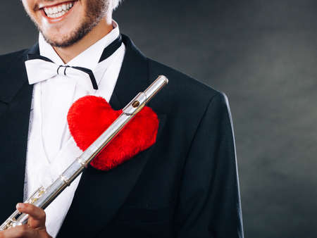 Valentines day love melody concept. Flute music playing male flutist musician performer. Young elegant stylish guy with instrument and red heartの写真素材