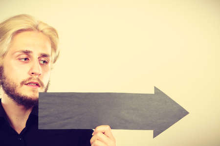 Planning, directions, choices concept. Man holding black arrow pointing right. Indoor shot on light backgroundの写真素材