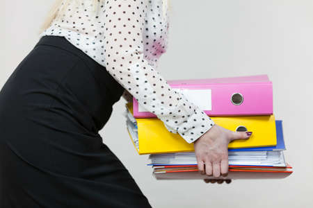 Woman holding many heavy colorful binders with documents. Office, bookkeeping objects concept.の写真素材