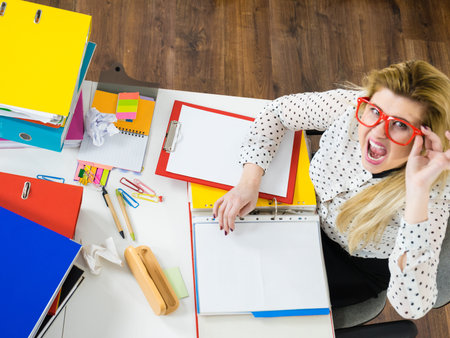 Shocked accountant business woman sitting working at desk full off documents in binders seeing...