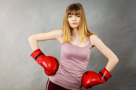 Sporty woman wearing red boxing gloves, fighting. Studio shot on grey, background.