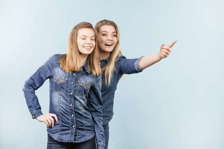Friendship, human relations concept. Two happy women friends or sisters wearing jeans shirts pointing somewhere.の写真素材
