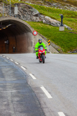 Tunnel entrance at the norwegian mountains and driver riding motorcycle on an empty asphalt roadの写真素材