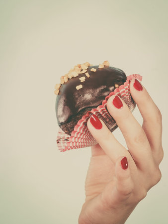 Diet, sweets, food concept. Woman hand holding delicious chocolate cupcake with peanut frosting...