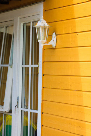 Rural, scandinavian architecture details concept. White window and antique lantern on yellow cottage made of wooden boards.の写真素材