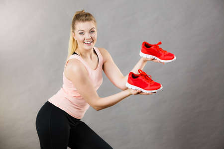 Happy sporty smiling woman presenting sportswear trainers red shoes, comfortable footwear perfect for workout and training.の写真素材