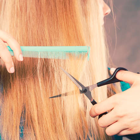 Cutting down and shearing concept. Blonde woman cuts and combing her straight smoothy fair hair. Professionalist making new coiffure hairdo.の写真素材