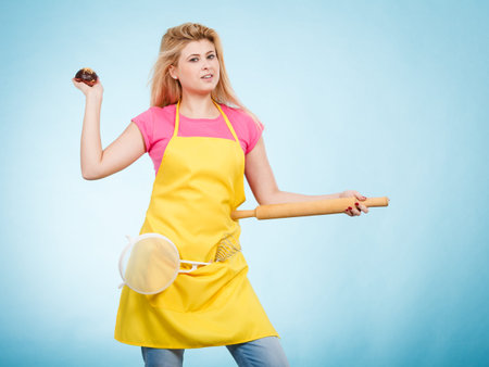 Baking tasty desserts sweets at home concept. Woman holding delicious chocolate cupcake, rolling pin and colander, wearing apronの写真素材