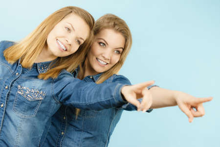 Friendship, human relations concept. Two happy women friends or sisters wearing jeans shirts pointing somewhere.の写真素材