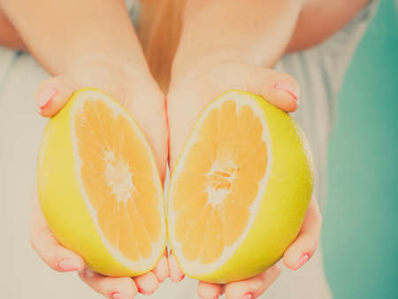 Halfs of yellow grapefruit citrus fruit in female hands closeup. Woman dietician recommend healthy diet nutrition.の写真素材