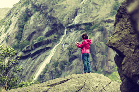 Woman on mountain rock enjoying beautiful nature view taking pictures. Adventure and traveling concept.の写真素材