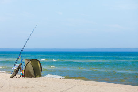 Fishing rod and tent left alone on beach shore of sea. Sunny summertime weather.の写真素材