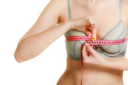 Woman slim girl in bra lingerie with red measure tape measuring her chest breasts. Closeup part of female body.の写真素材