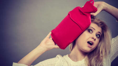 Woman holding red hot water bottle on head to deal with headacheの写真素材