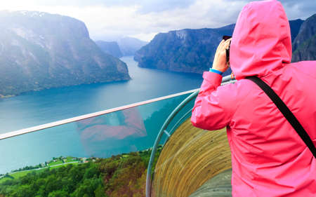 Tourism and travel. Woman tourist nature photographer taking photo with camera, enjoying Aurland fjord landscape from Stegastein lookout, Norway Scandinavia.の写真素材