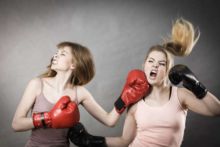 Two agressive women wearing boxing gloves having argue fight being mad at each other. Female violance concept.の写真素材