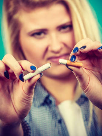 New Year resolutions, bad habits, unhealthy lifestyle concept. Woman breaking cigarette, getting rid of addictionの写真素材