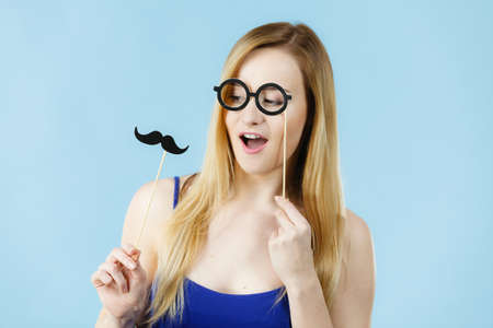 Woman holding carnival accessoies on stick having fun. Studio shot on blue background.の写真素材