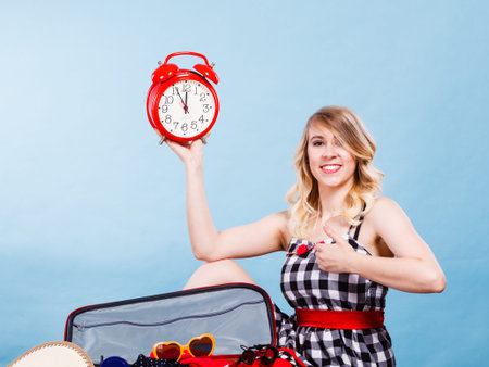 Time for travel concept. Happy woman sitting on floor with messy packed suitcase holding big red old...