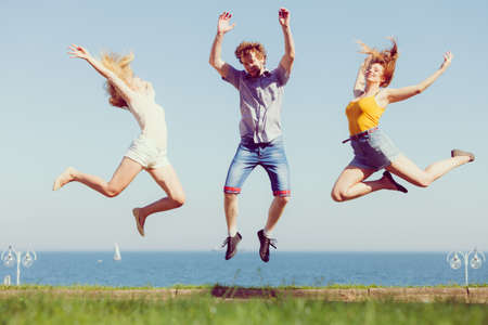 Friendship freedom summer holidays concept. Group of friends boy two girls jumping outdoor against skyの写真素材