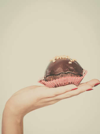 Diet, sweets, food concept. Woman hand holding delicious chocolate cupcake with peanut frosting about to take biteの写真素材