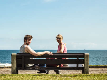 Couple man and woman dating by sea ocean outdoor. Young girl and guy sitting on bench. Summer love.の写真素材