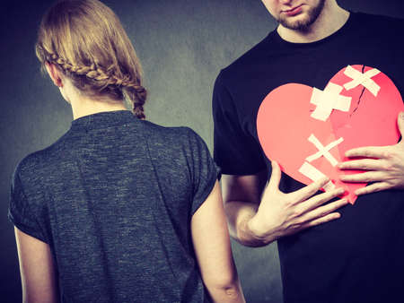 Broken heart difficult love concept. Sad unhappy couple woman and man holding paper red heart fixed with plaster bandage. Rift in relations.の写真素材