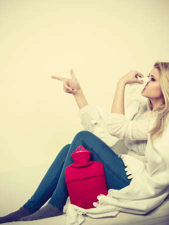 Sickness, seasonal virus problem concept. Woman being sick having flu lying on sofa sneezing into tissue pointing at copyspaceの写真素材