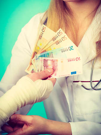 Corruption in healthcare industry. Female doctor bandaging male hand. Man giving money to woman. Bribery in medicine.のeditorial素材