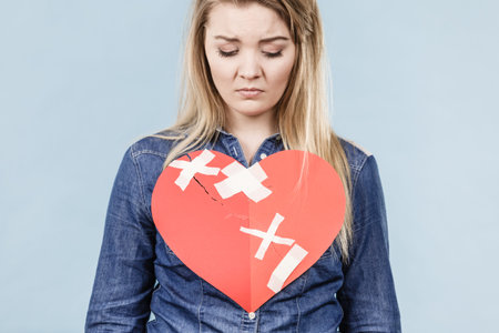 Sad young teenage woman with broken heart made of paper. Negative sad emotions, relationship...
