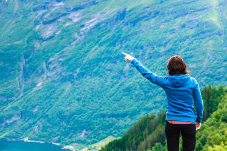 Travel concept. Tourist woman looking and pointing with finger at fjords beautiful mountains landscape in Norwayのeditorial素材