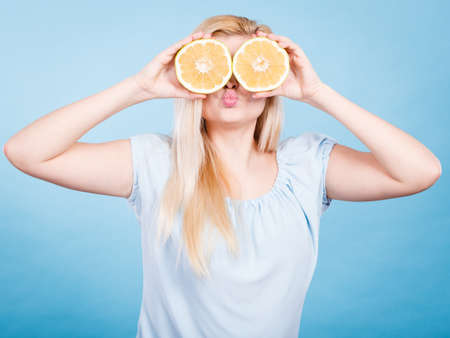 Woman blonde teen girl holding two halfs of yellow grapefruit citrus fruit in hands, covering her eyes, on blue. Healthy diet nutrition. Happiness fun concept.のeditorial素材