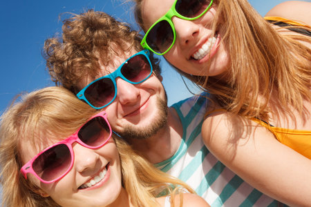 Friendship happiness summer holidays concept. Group of friends boy two girls in colorful sunglasses...