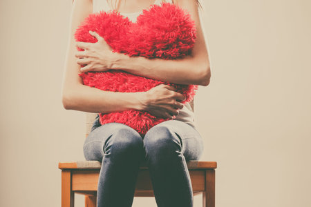 Broken heart love concept. Sad unhappy woman hugging red heart pillowの写真素材