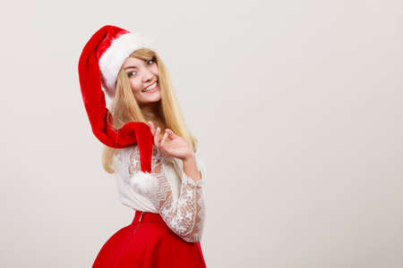 Happy smiling cute woman in santa helper hat. Pretty blonde girl in studio on gray. Christmas xmas season.の写真素材