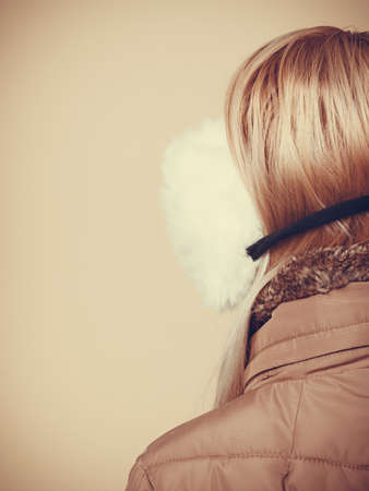 Accessories and clothes for cold days, fashion concept. Blonde woman in winter warm earmuffs and jacket, view from back.の写真素材
