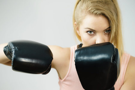 Sporty woman wearing black boxing gloves, fighting. Studio shot on grey background.