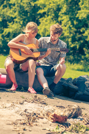 Adventure, tourism, enjoying summer time together - young couple tourists having fun playing guitar...