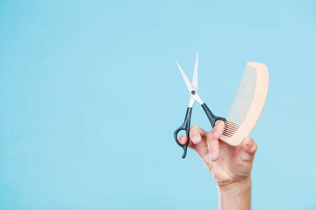 Style and fashion. Male hand of hairstylist barber holds scissors and wooden comb, creating hairdo coiffureの写真素材