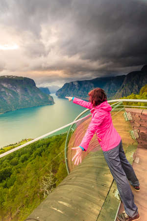 Tourist woman on Stegastein viewpoint enjoying Aurland fjord view in evening time, Sogn Og Fjordane, Norwayの写真素材