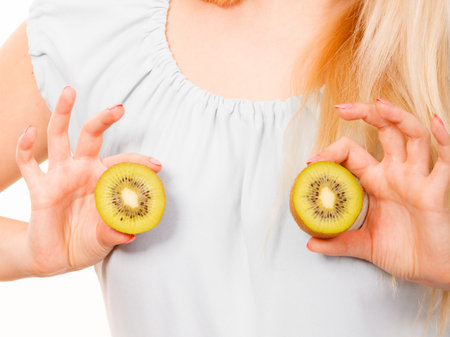 Healthy diet, refreshing food full of vitamins. Woman holding sweet delicious green kiwi fruit on breastの写真素材