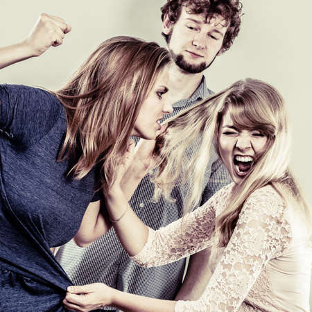 Aggressive mad women fighting over man pulling hair. Young jealous girls wooing guy. Violence.の写真素材