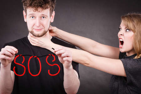 Betrayal and break up in relationship. Young couple arguing and holding red sos word sign symbol. Blonde woman in fury yelling on man. Negative emotions.の写真素材