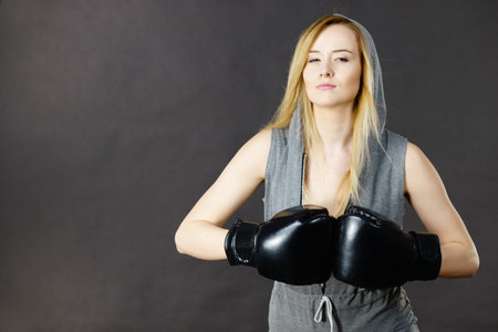 Young hooded woman fighting boxing. Blonde attractive girl wearing black punch gloves. Sport and...