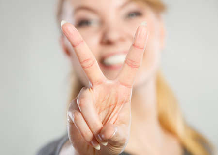 Celebration communication success concept. Cheerful lady makes v gesture. Young girl showing peace sign victory symbol.の写真素材