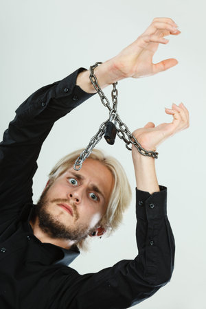 No freedom, social problems concept. Sad man with chained hands, studio shot on light grey backgroundの写真素材