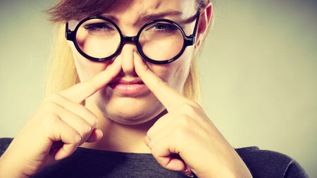 Bad smell concept. Young woman feels disgust pinches her nose with fingers because of odor stench...