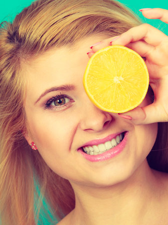 Woman teen girl holding half of yellow lemon citrus fruit in hand, covering her eye, on green. Healthy diet nutrition. Happiness fun concept.の写真素材