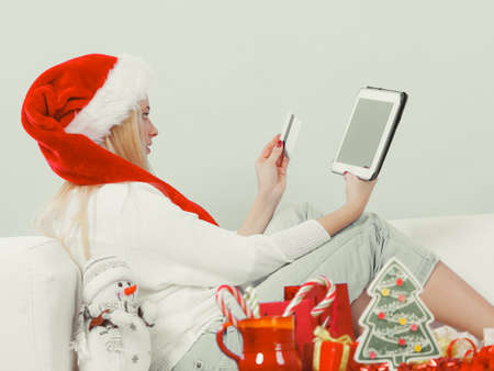 Christmas time concept. Young woman teen girl with tablet pc laptop and credit card on sofa at home doing online shopping, buying browsing for gifts, having funの写真素材